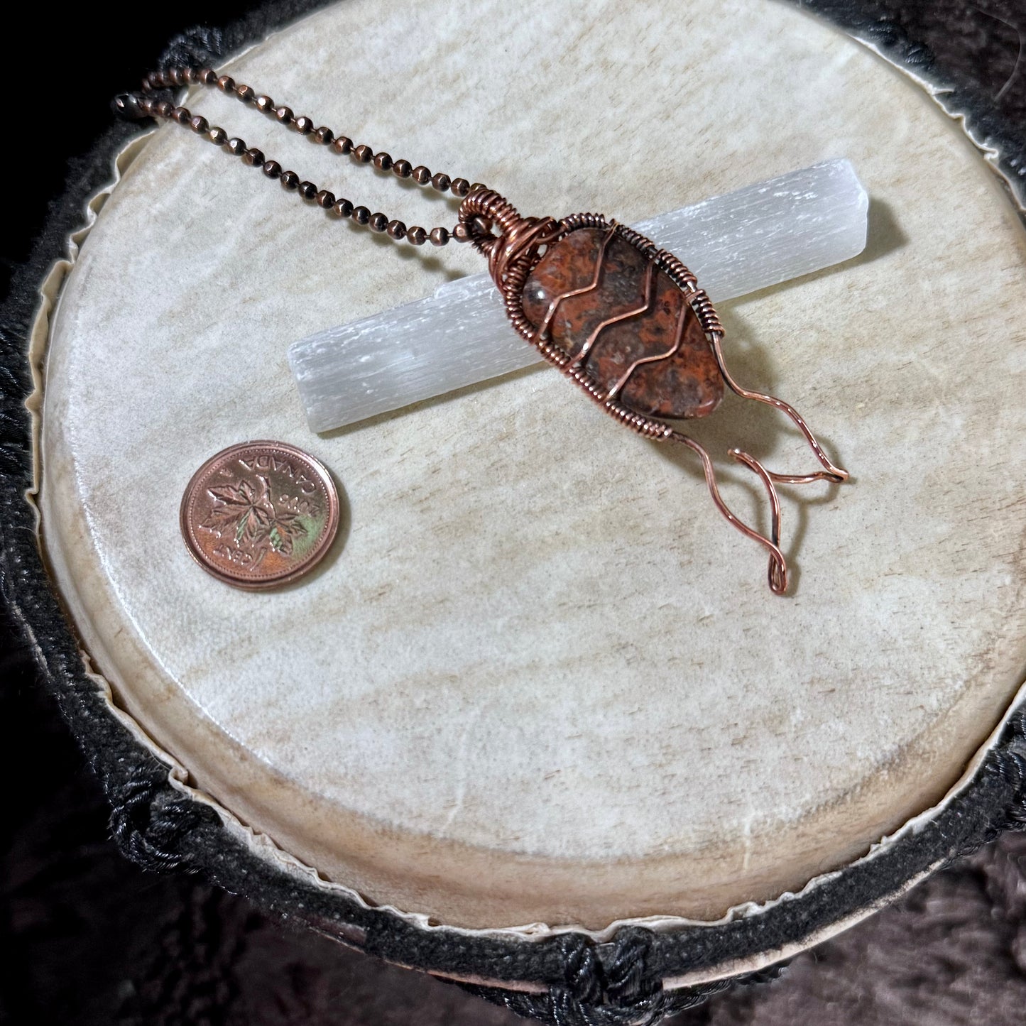 Leopard Skin Jasper Mermaid Tail Necklace displayed with a selenite wand and Canadian penny for scale, highlighting the natural gemstone, reclaimed copper wire wrapping, and one-of-a-kind artisan craftsmanship.