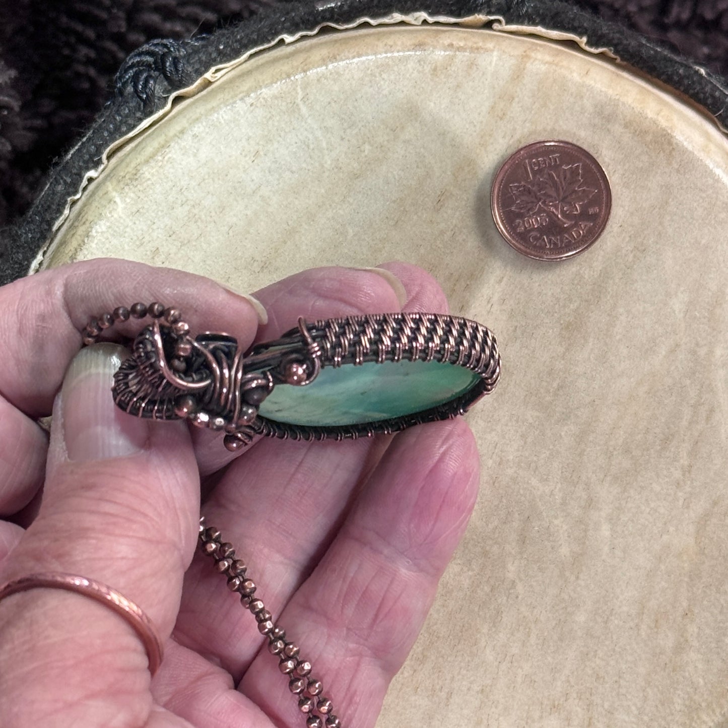 Close-up of the side profile of a handmade agatized chrysoprase pendant in patinated copper shown in hand for scale.