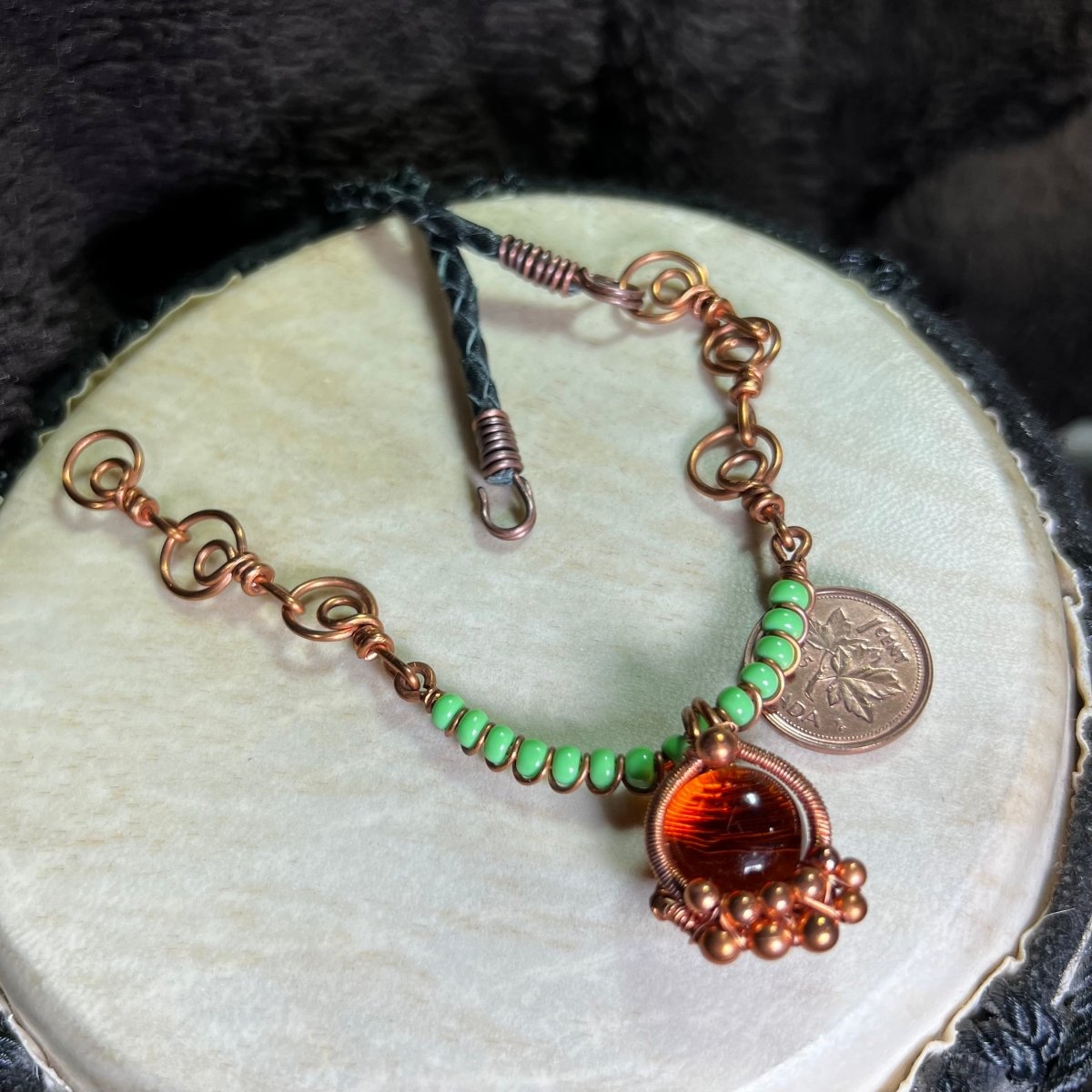 Necklace with green beads and an orange glass cabochon wrapped in raw copper, on a white surface, next to a penny for scale.