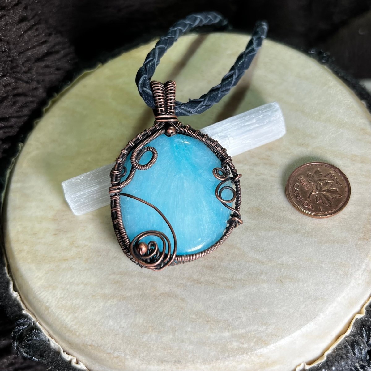Blue Aragonite pendant with copper wire wrapping on a beige surface next to a penny for scale.