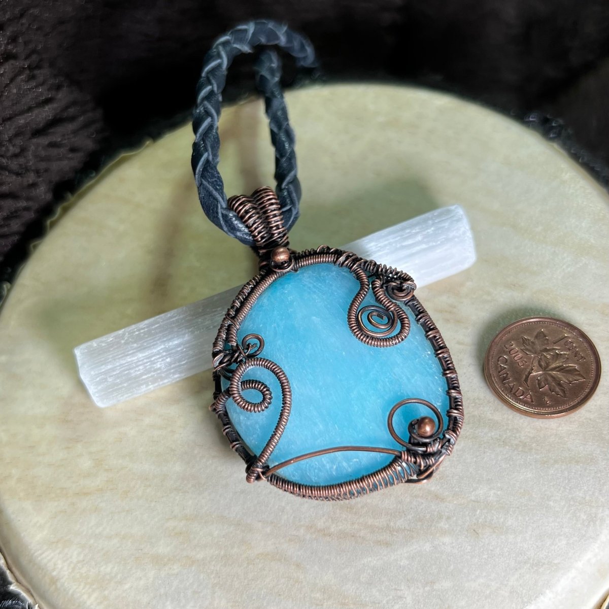 Blue Aragonite pendant with copper wire wrapping on a beige surface next to a penny for scale.