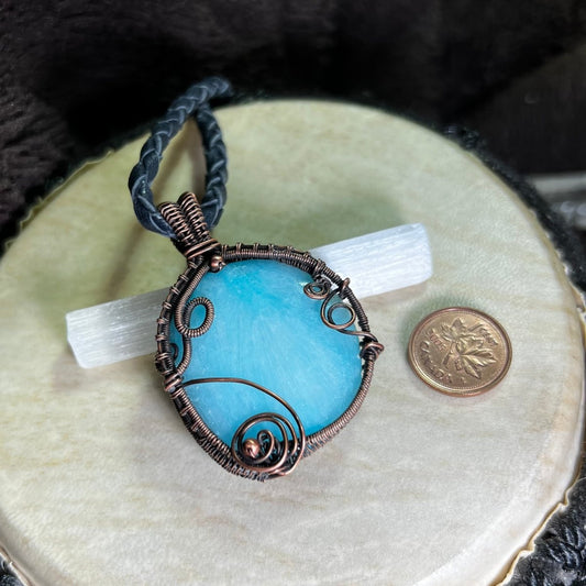 Blue Aragonite pendant with copper wire wrapping on a beige surface next to a penny for scale.