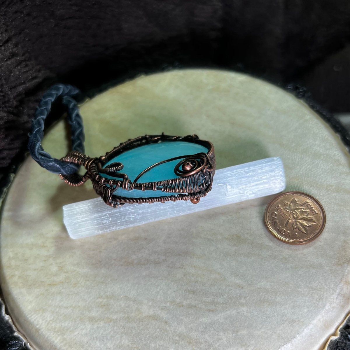 Blue Aragonite pendant side view with copper wire wrapping on a beige surface next to a penny for scale.
