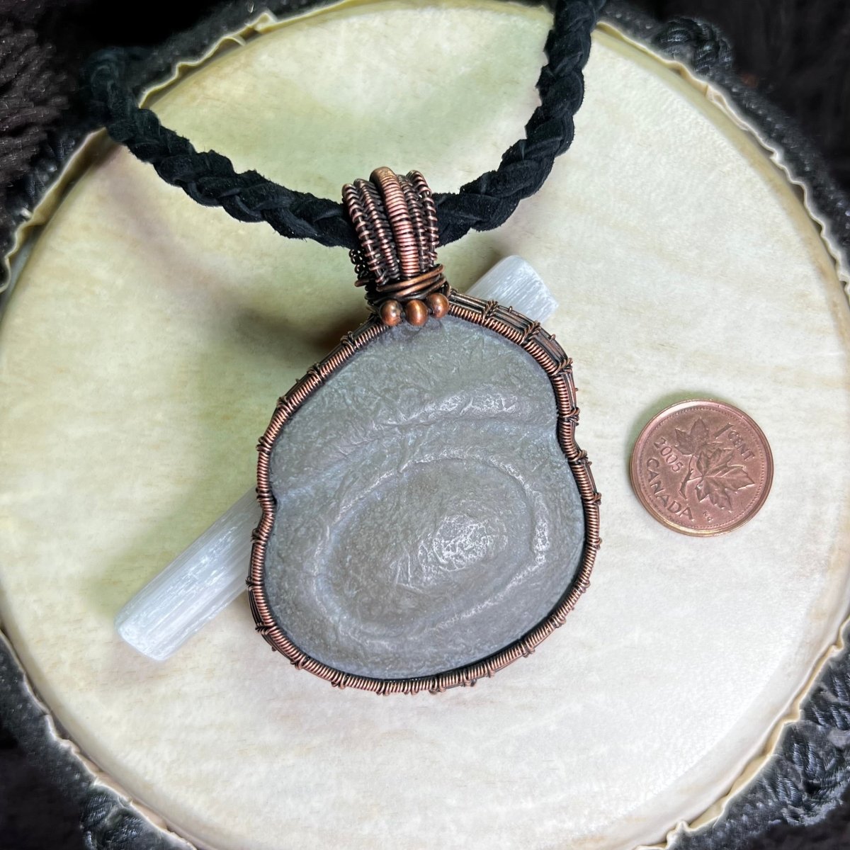 Necklace with a large Canadian Fairy Stone pendant wrapped in copper on a white background next to a penny for scale.