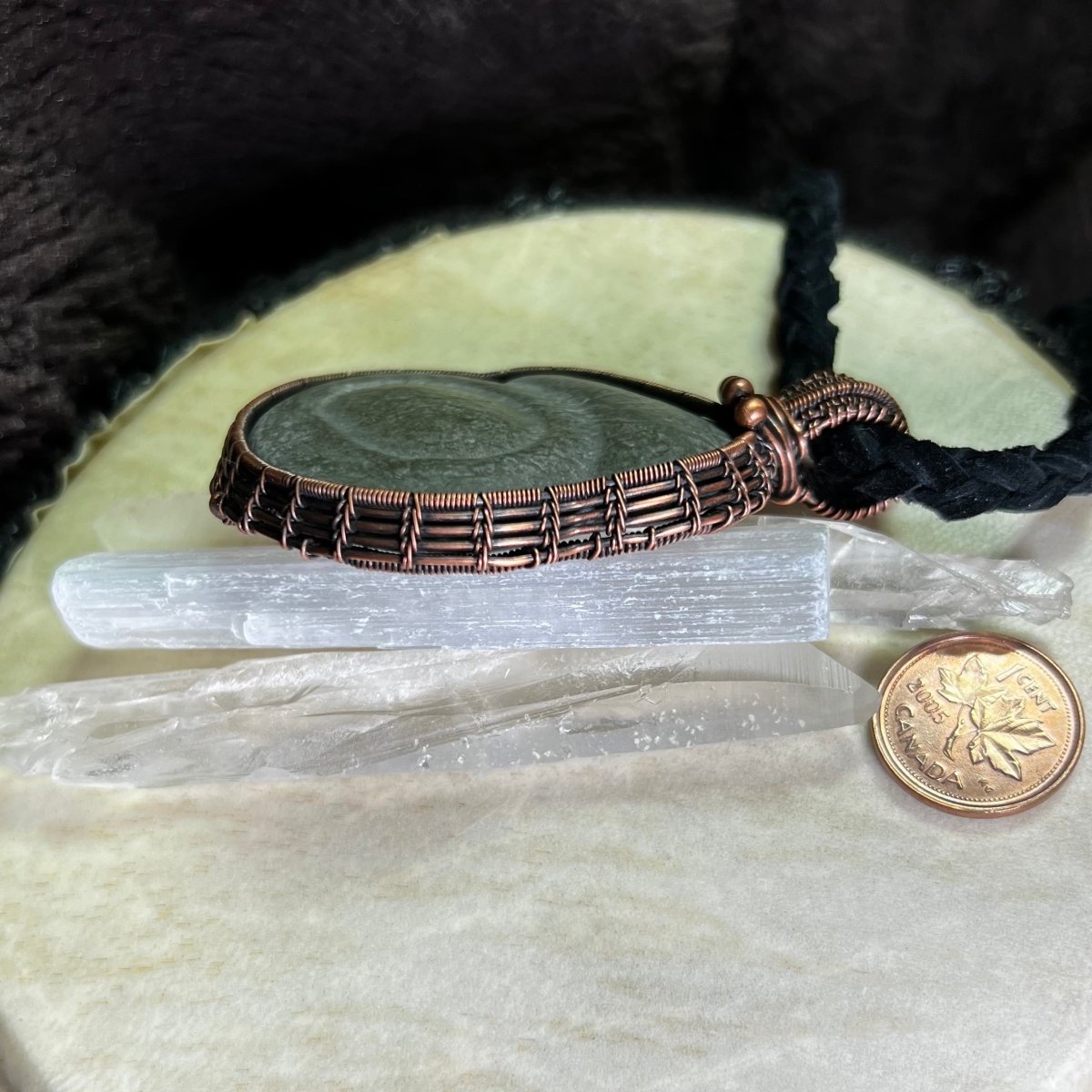 Copper wire-wrapped pendant with selenite sticks on a black and white background