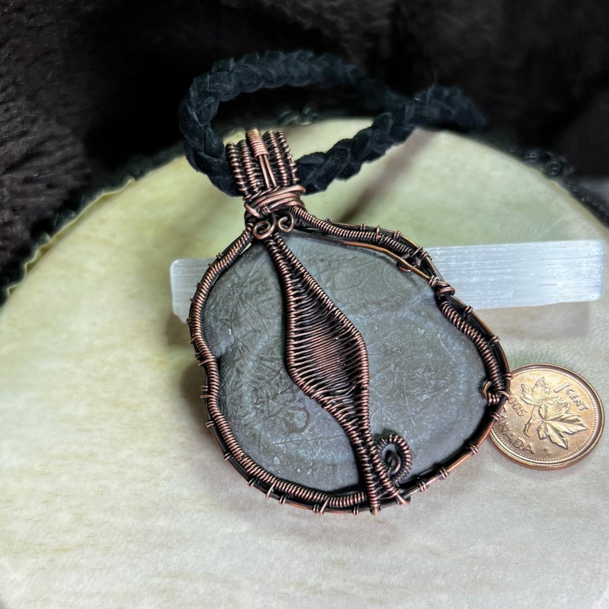 Back view of a necklace with a large Canadian Fairy Stone pendant wrapped in copper on a white background next to a penny for scale.