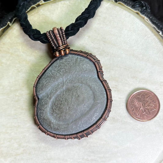 Necklace with a large Canadian Fairy Stone pendant wrapped in copper on a white background next to a penny for scale.