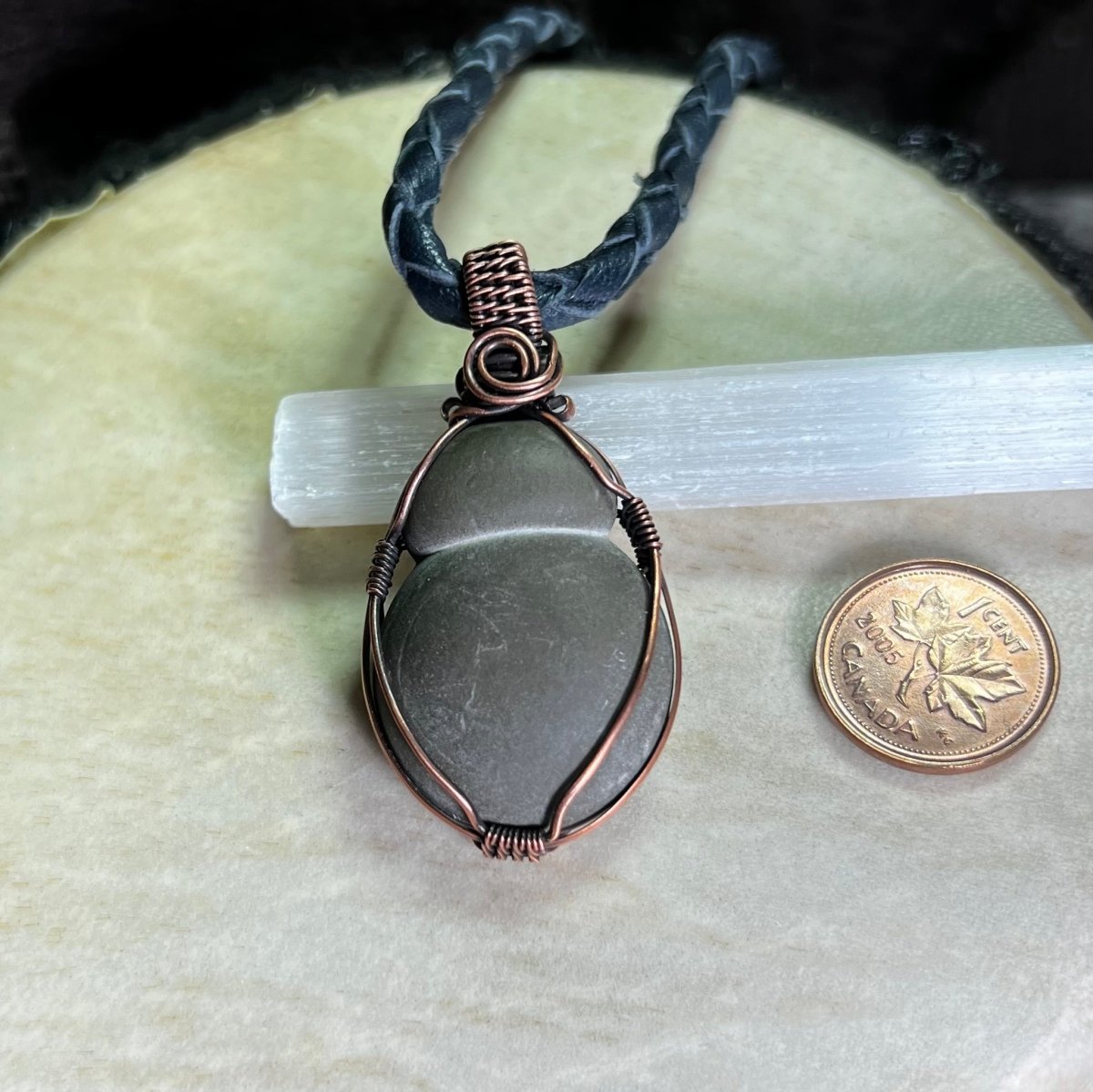 Necklace with a pendant on a white stone, next to a penny for scale.