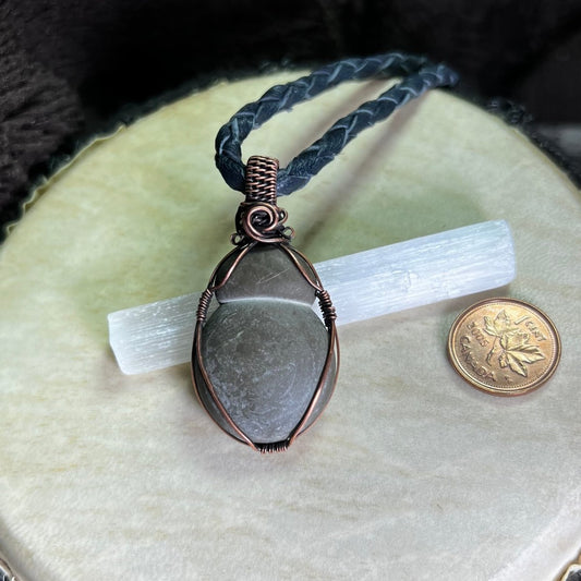 Necklace with a bulbous teardrop-shaped Canadian Fairy Stone wrapped in copper on a cream surface, next to a penny for scale.