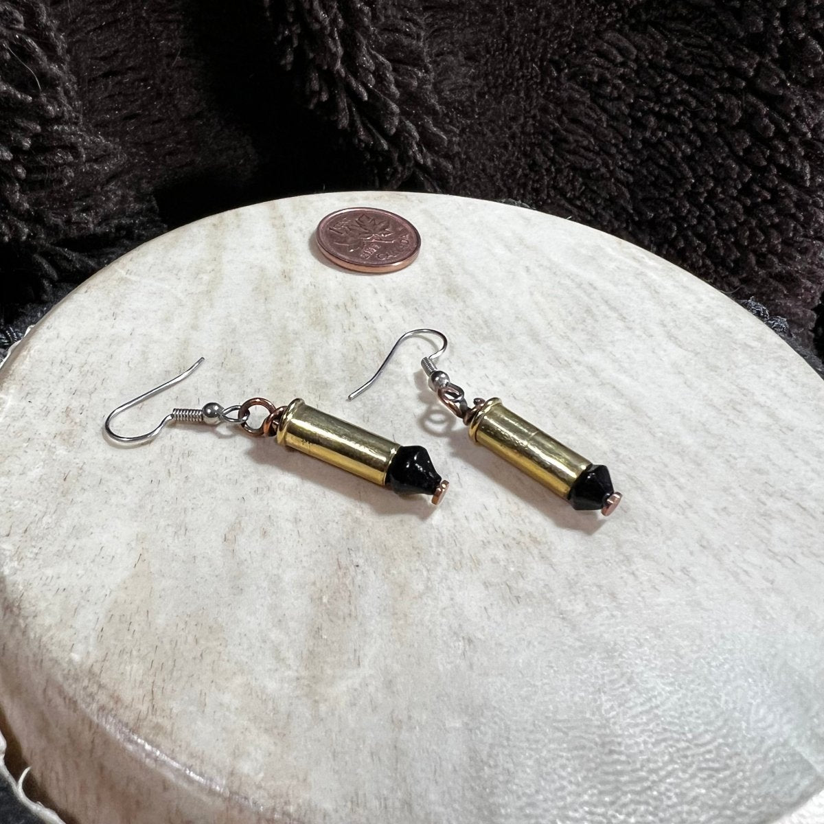 Pair of reclaimed 22 shells earrings with black beads on a round beige surface with a penny coin for scale.