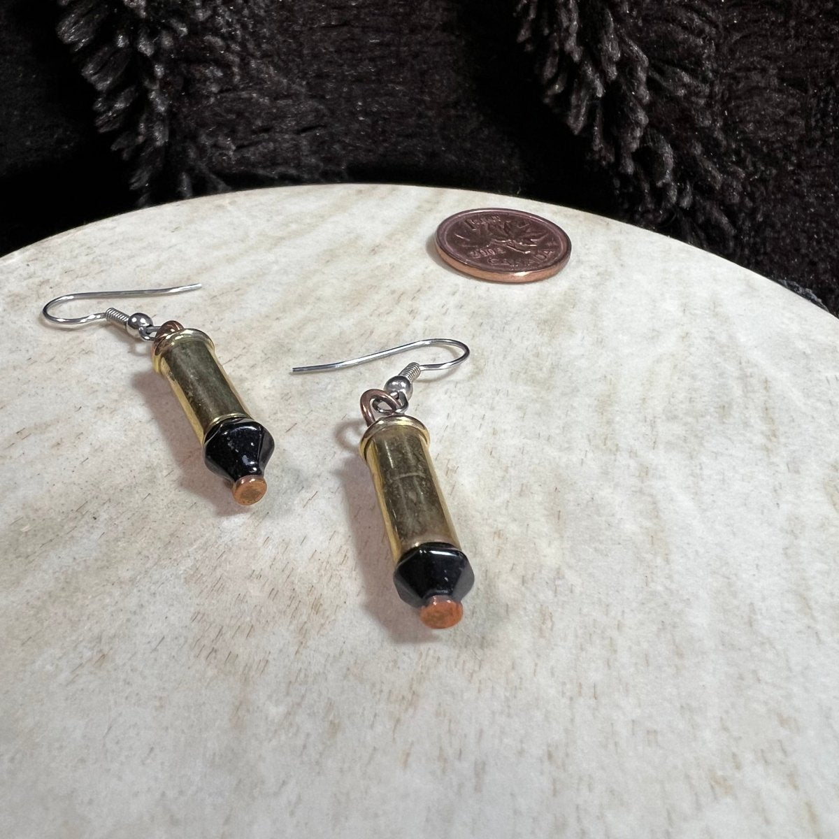 Pair of reclaimed 22 shells earrings with black beads on a round beige surface with a penny coin for scale.