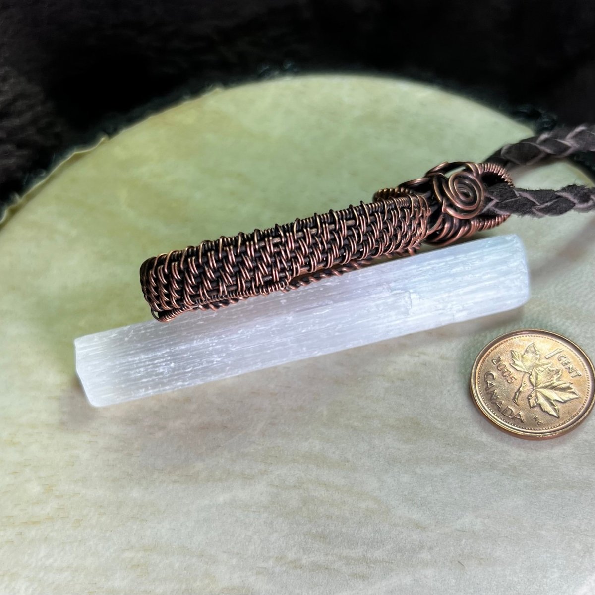 Side view of a necklace with a peach celestobarite stone wrapped in copper on a cream surface next to a penny for scale.