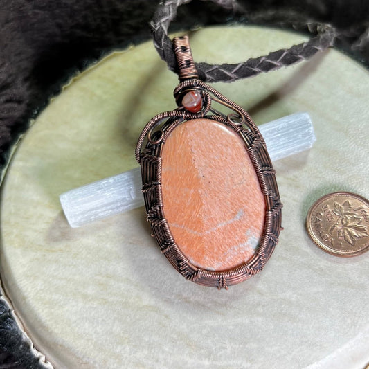 Copper wrapped necklace with a peachy celestobarite stone pendant on a cream coloured surface next to a penny for scale
