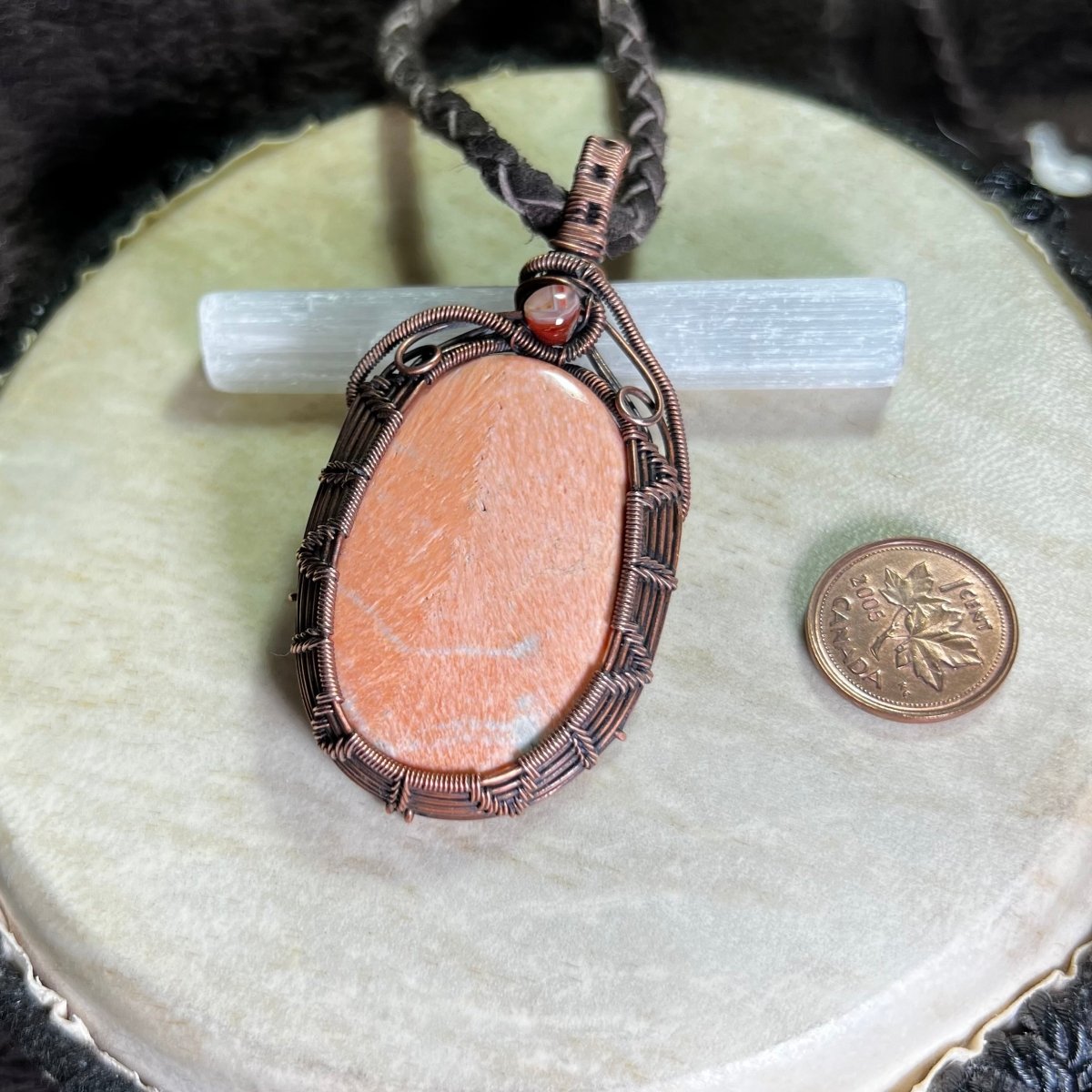 Necklace with a peach stone pendant on a white surface next to a penny for scale