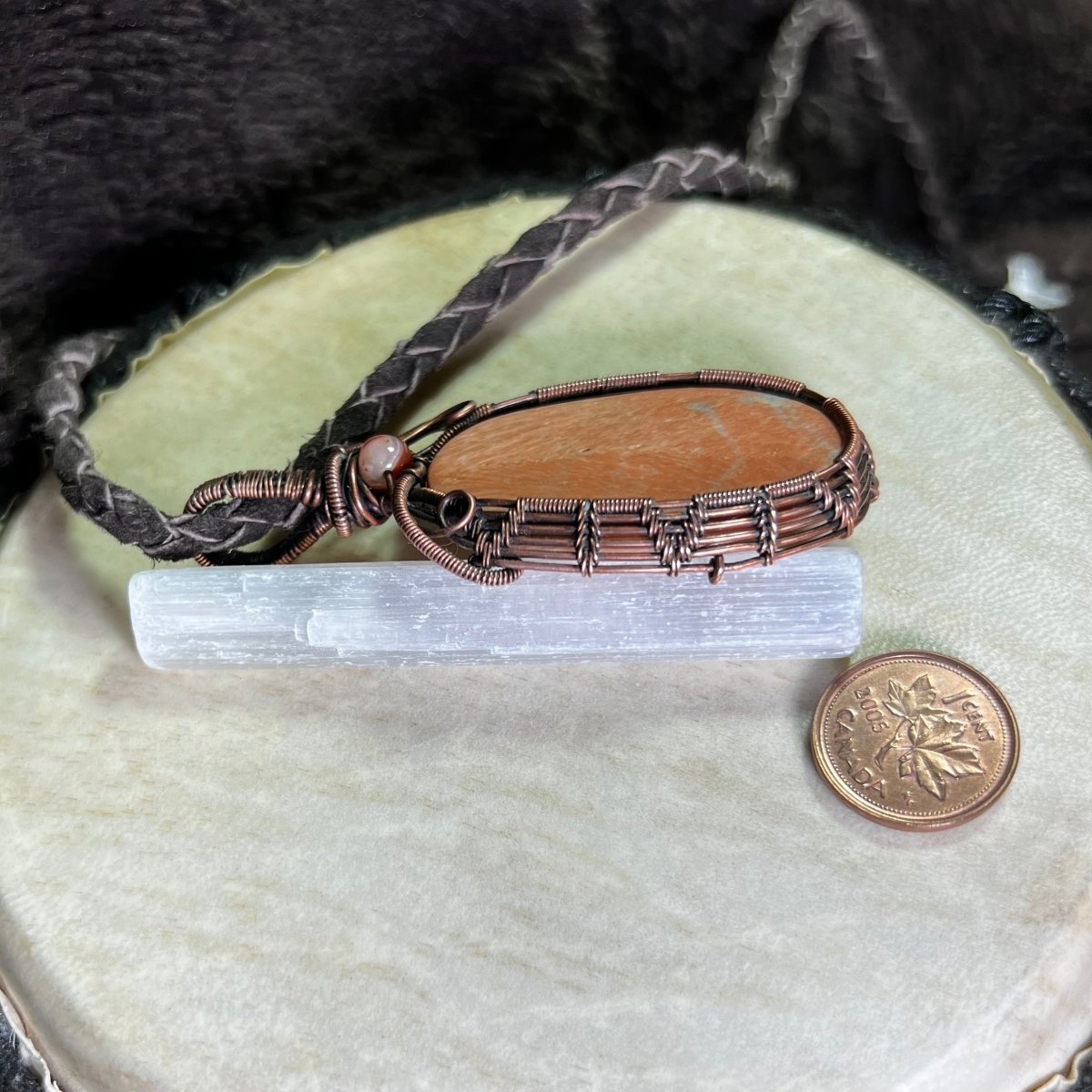 copper wire wrapped celestobarite pendant leaning against a selenite stick next to a penny for scale