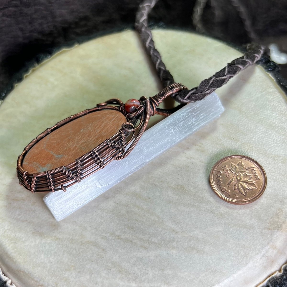 Celestobarite copper wrapped necklace on a cream coloured surface next to a penny for scale.