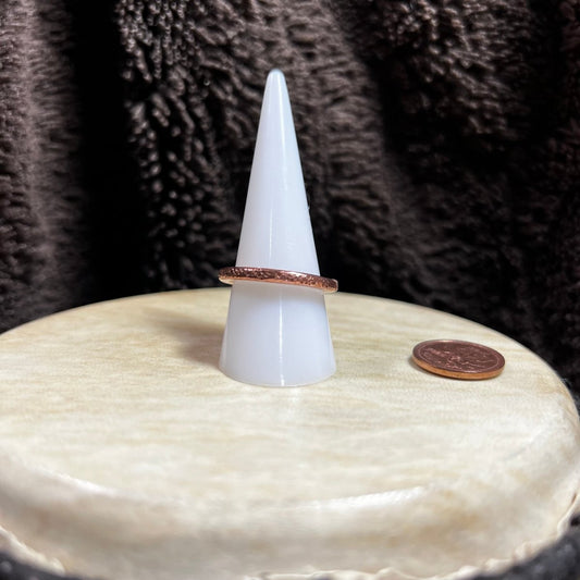 Copper band ring on a white ring stand on a textured surface next to a penny for scale.