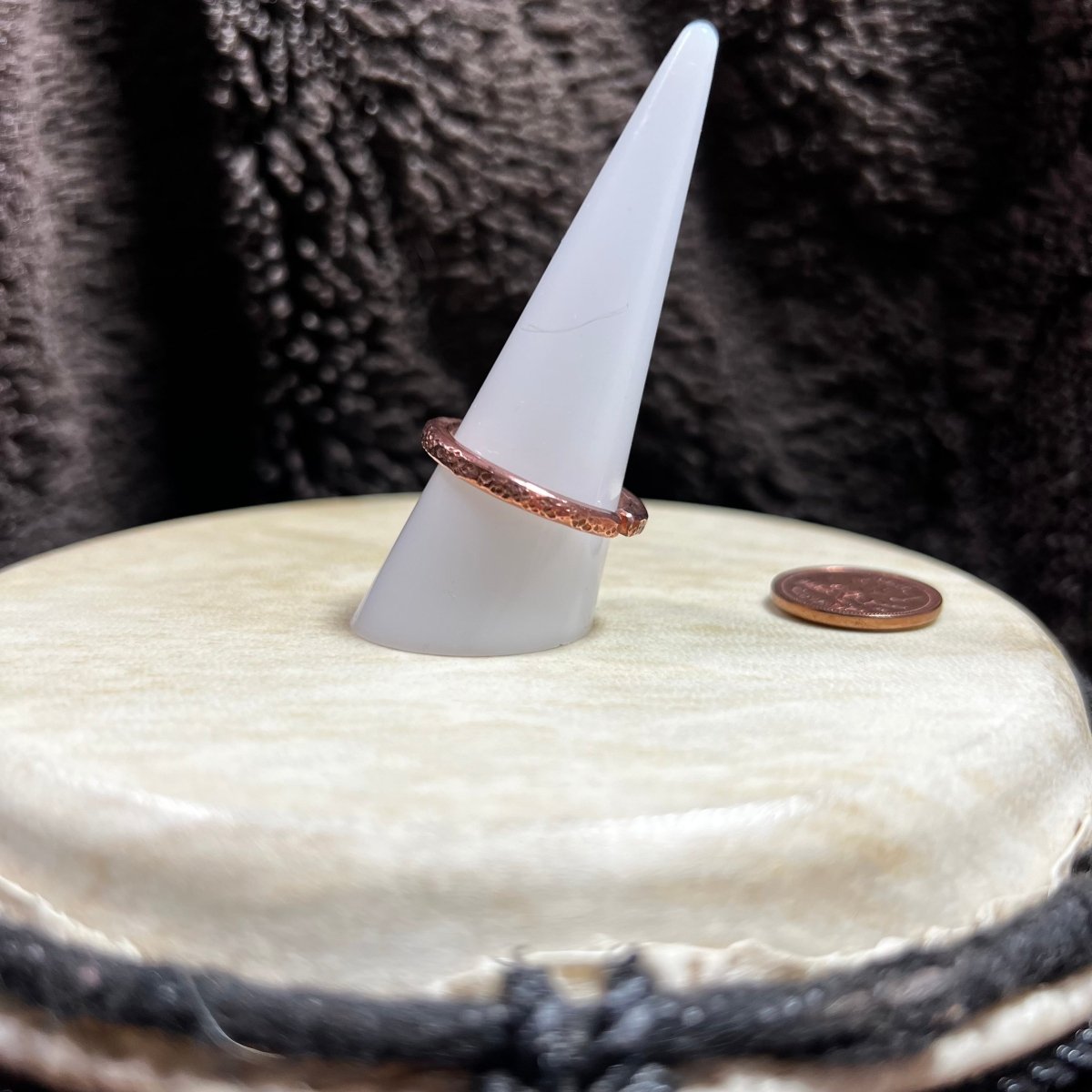 Copper band ring on a white ring stand on a textured surface next to a penny for scale.