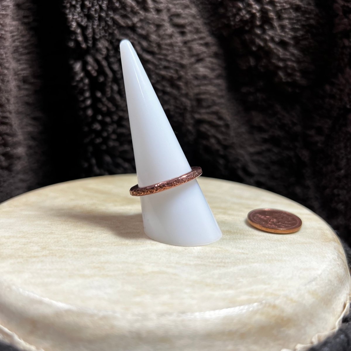 Copper band ring on a white ring stand on a textured surface next to a penny for scale.