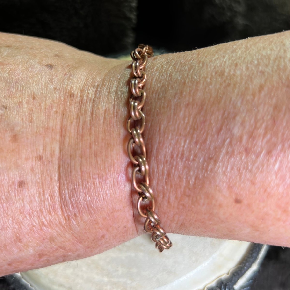 Copper chain link bracelet on a wrist with a blurred background