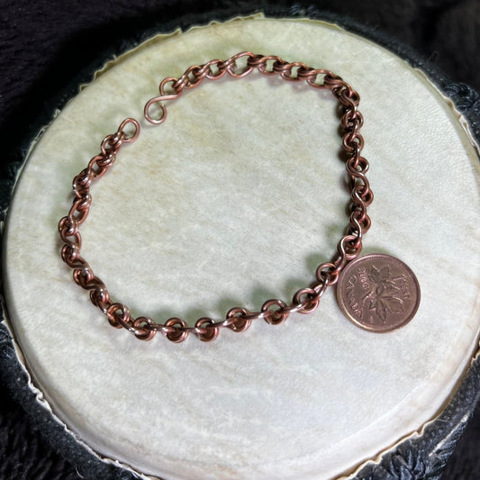 Copper chain bracelet next to a penny for scale on a textured surface
