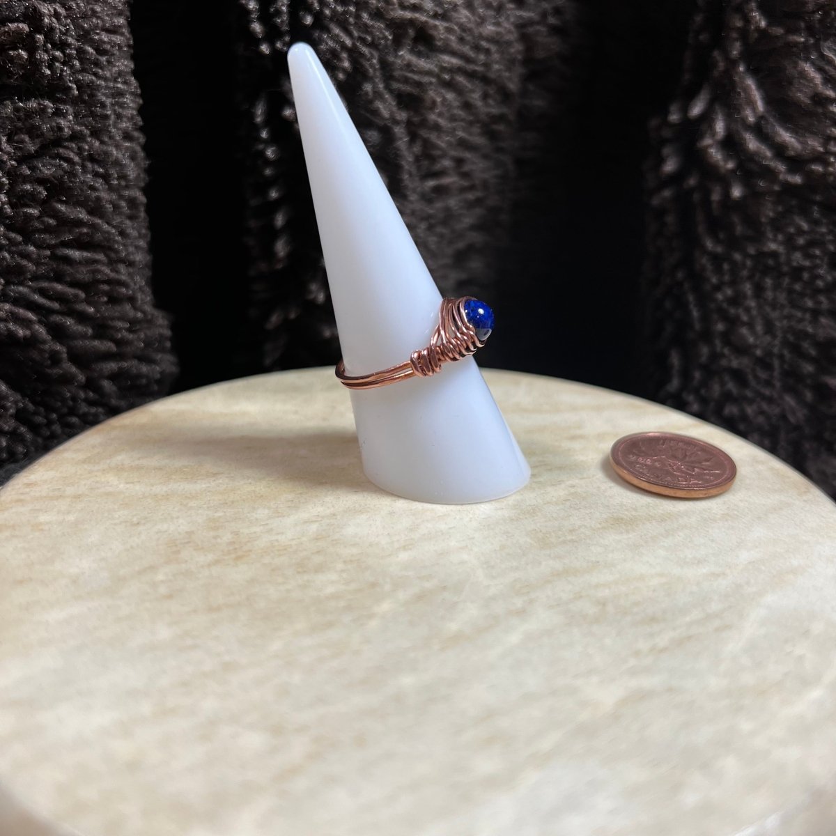 Ring with a blue stone on a white cone-shaped stand next to a penny for scale.