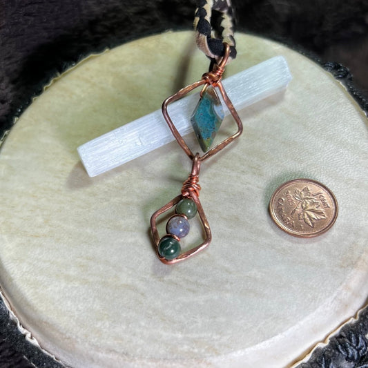 Copper wire-wrapped pendant with moss agate stones on a white surface next to a penny for scale.