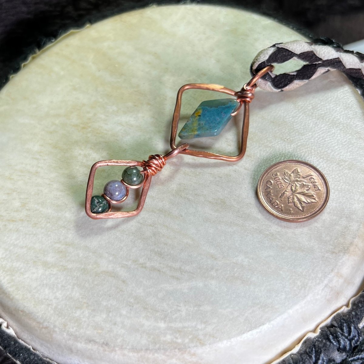 Necklace with geometric copper design and moss agate stones on a white surface, next to a penny for scale.