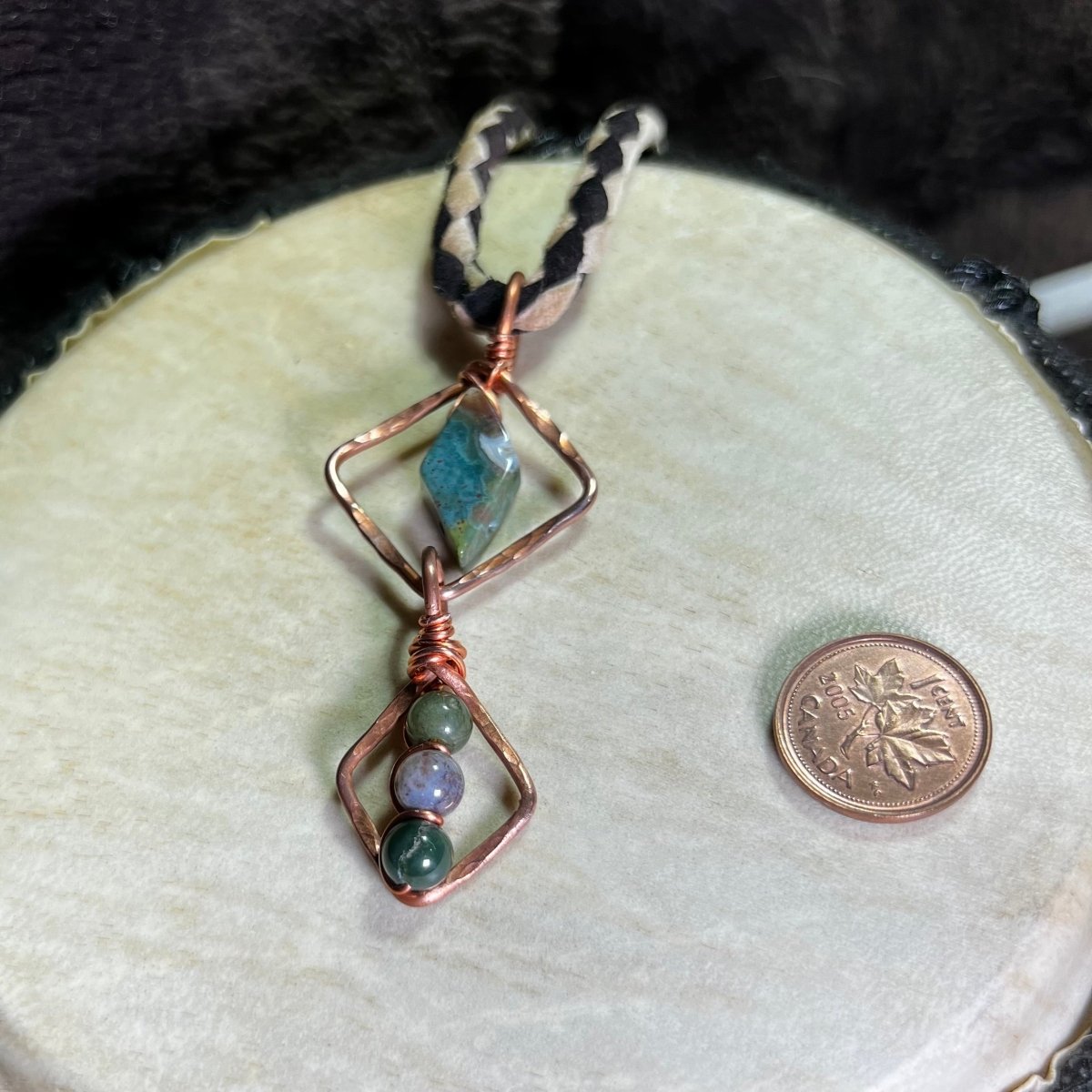 Necklace with geometric copper design and moss agate stones on a white surface, next to a penny for scale