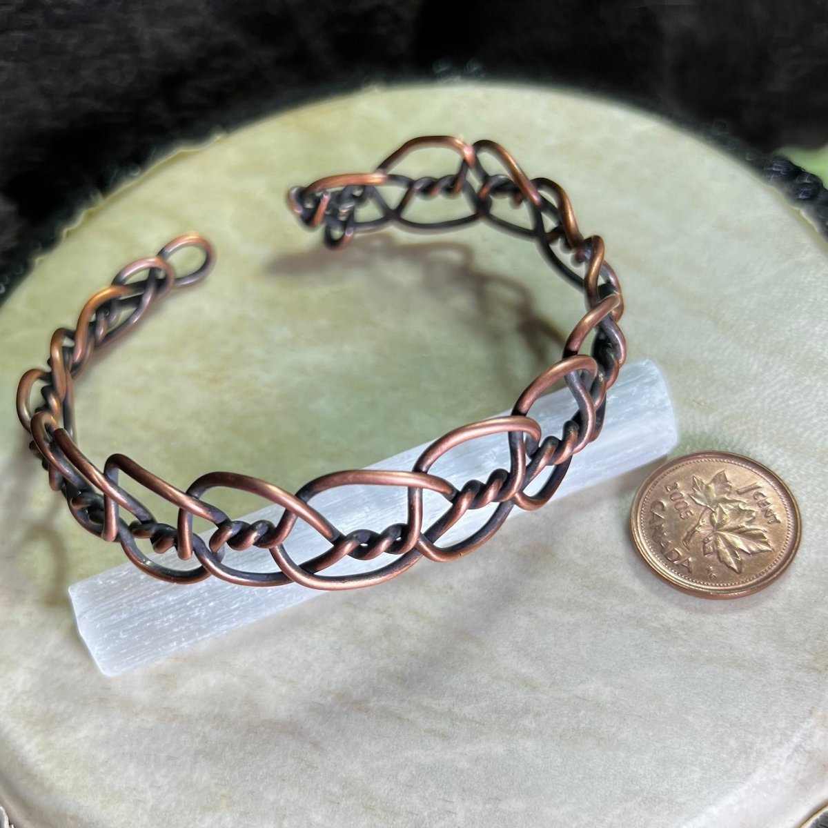Copper bracelet on a white surface with a coin for scale