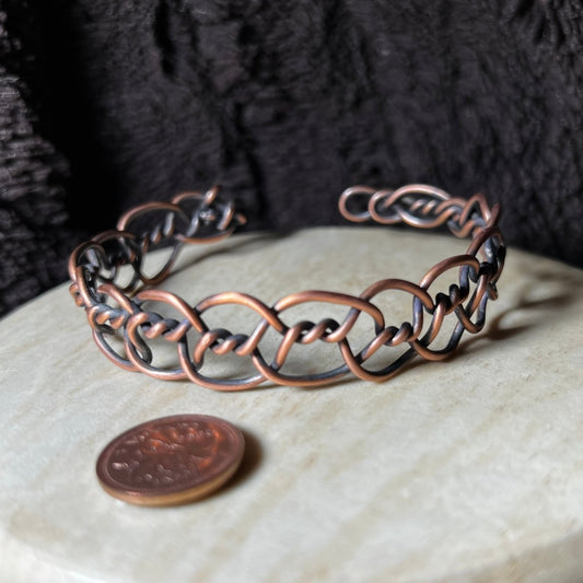 Copper bracelet on a beige surface with a penny for scale