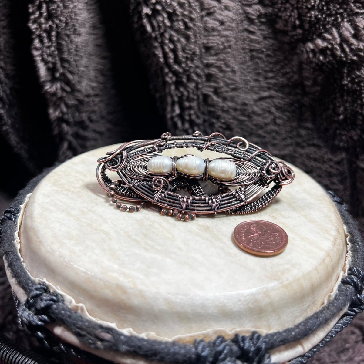 Decorative necklace with pearls on a white surface, next to a penny for scale