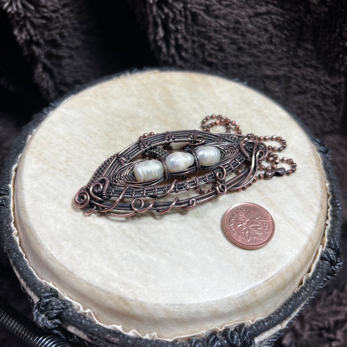 Decorative necklace with pearls on a round surface next to a penny.