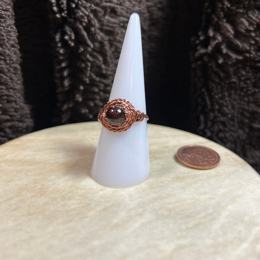Ring with deep red garnet stone on a white cone-shaped stand against a textured dark background