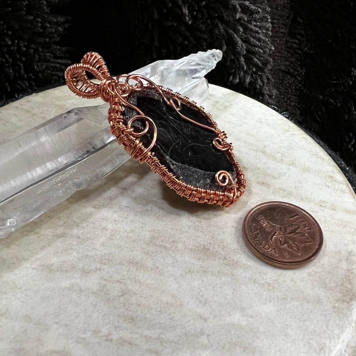 Copper wire-wrapped garnet slice pendant on a neutral surface next to a Canadian penny for scale.