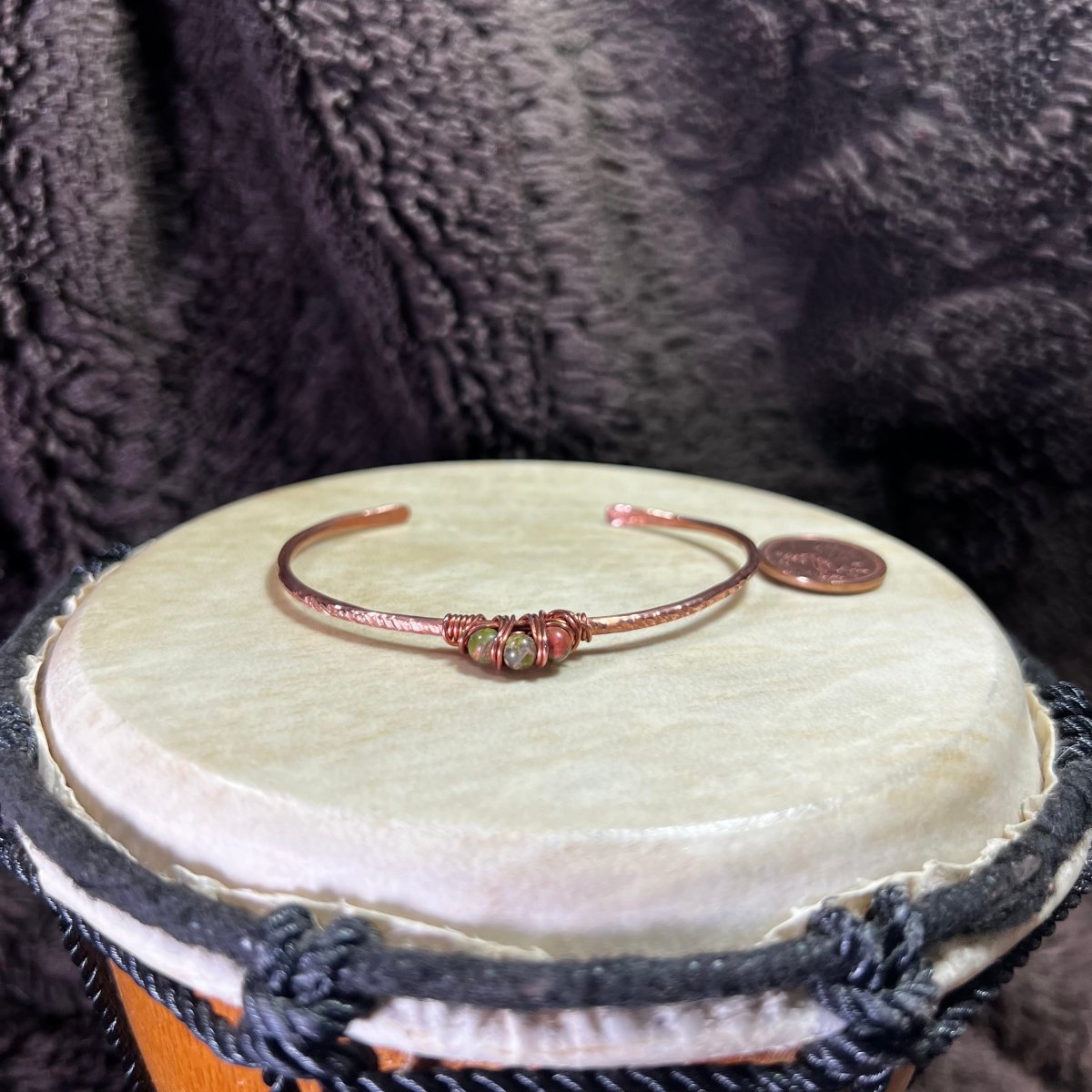 Copper bracelet with unakite stones on a wooden drum against a dark textured background