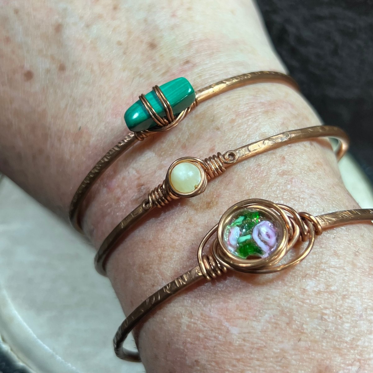 Three copper bracelets with green and yellow stones on a wrist.
