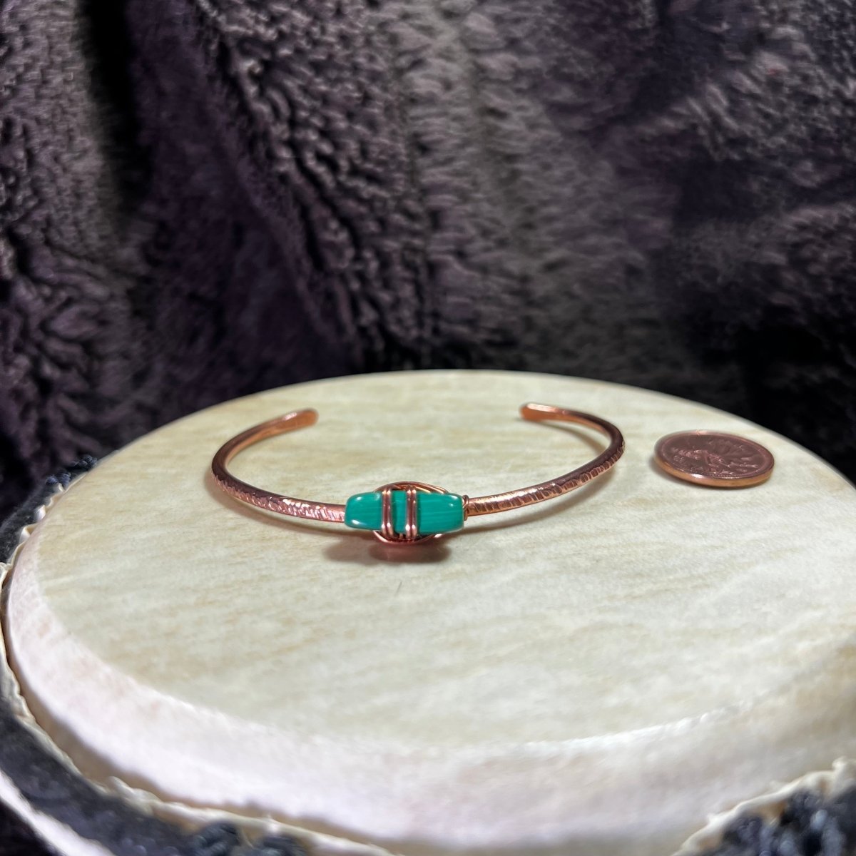 Copper Bracelet with a green malachite stone on a round white surface with a coin for scale.