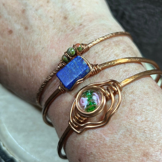 Close-up of a wrist wearing three copper bracelets with gemstones.
