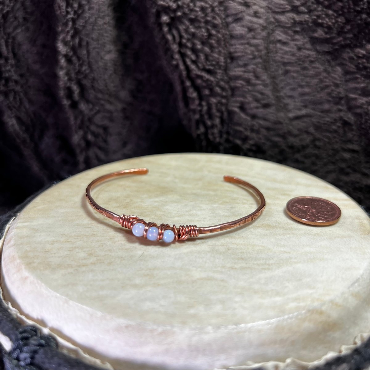 Copper bracelet with blue lace agate stones on a round beige surface, next to a penny for scale.