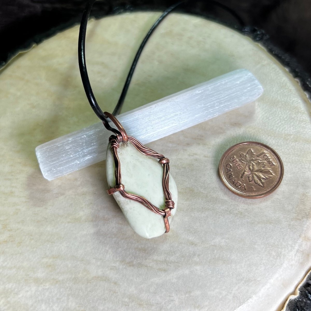 Necklace with a lemon chrysoprase stone pendant on a selenite crystal and next to a penny for scale.
