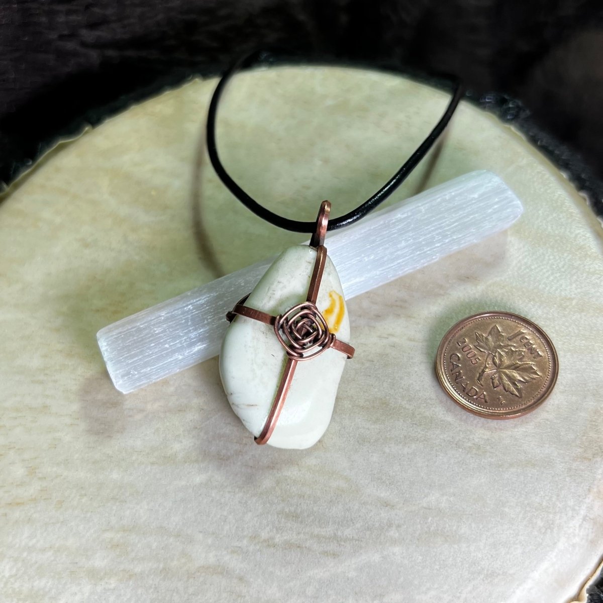 Necklace with a lemon chrysoprase stone pendant on a selenite crystal and next to a penny for scale.