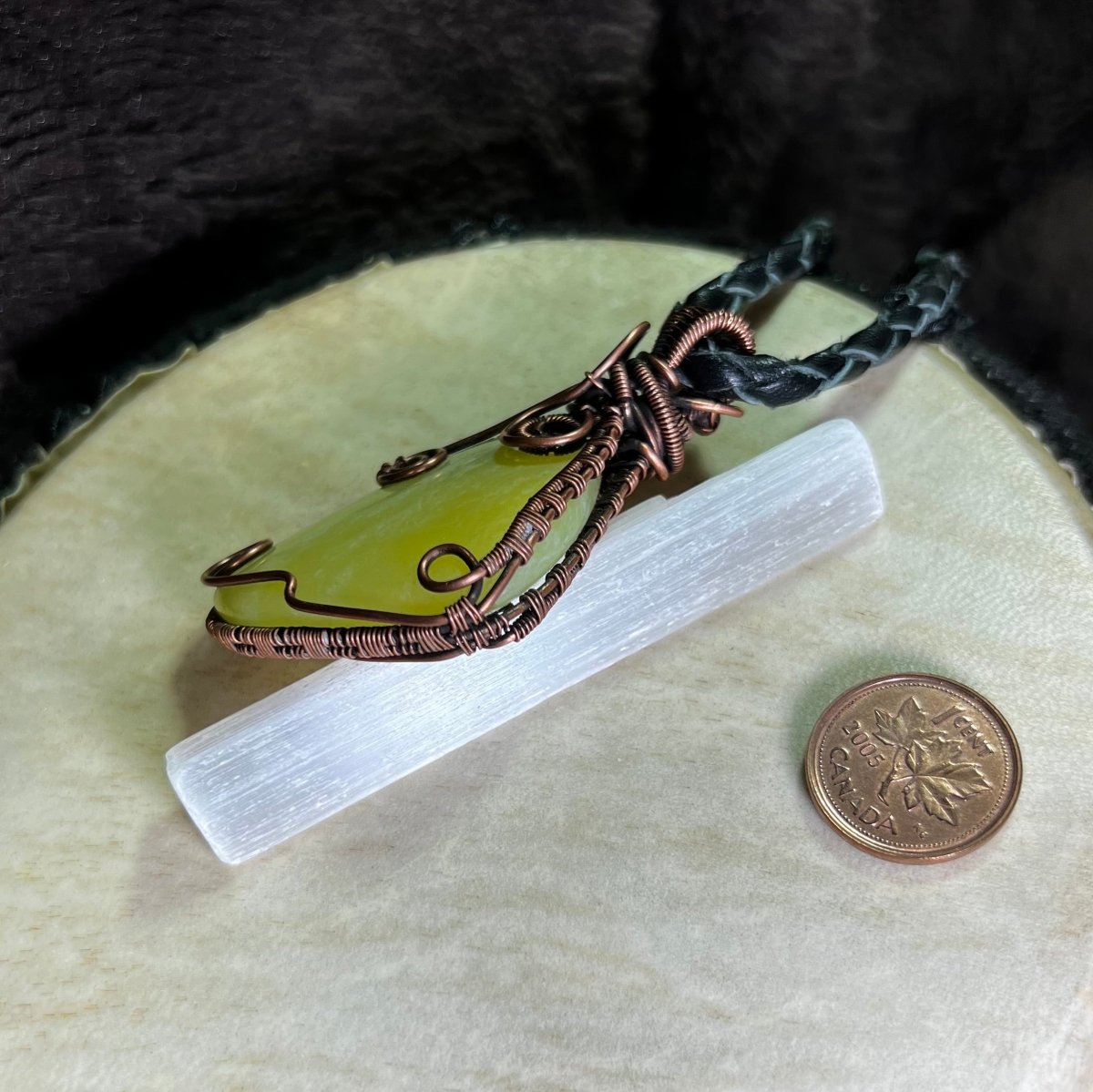 Lemon Jade stone pendant with copper wire wrapping on a white surface, next to a penny for scale.