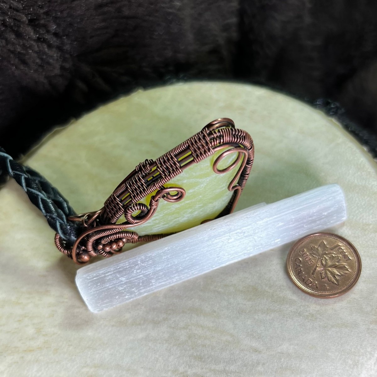Lemon Jade stone pendant with copper wire wrapping on a white surface, next to a penny for scale.