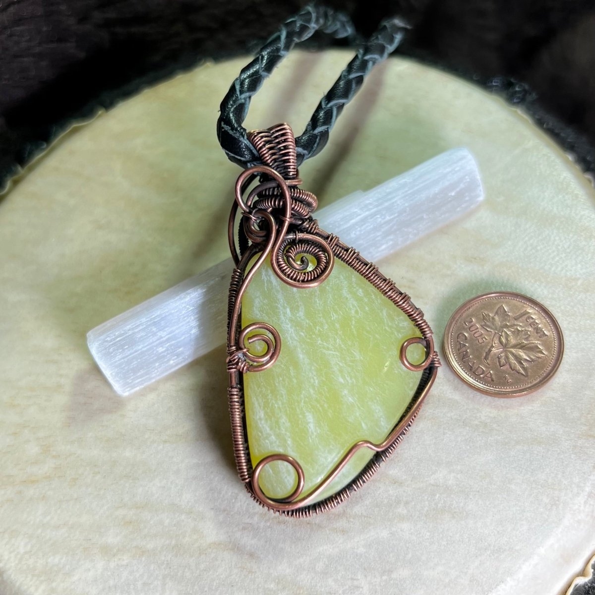 Lemon Jade stone pendant with copper wire wrapping on a white surface, next to a penny for scale.