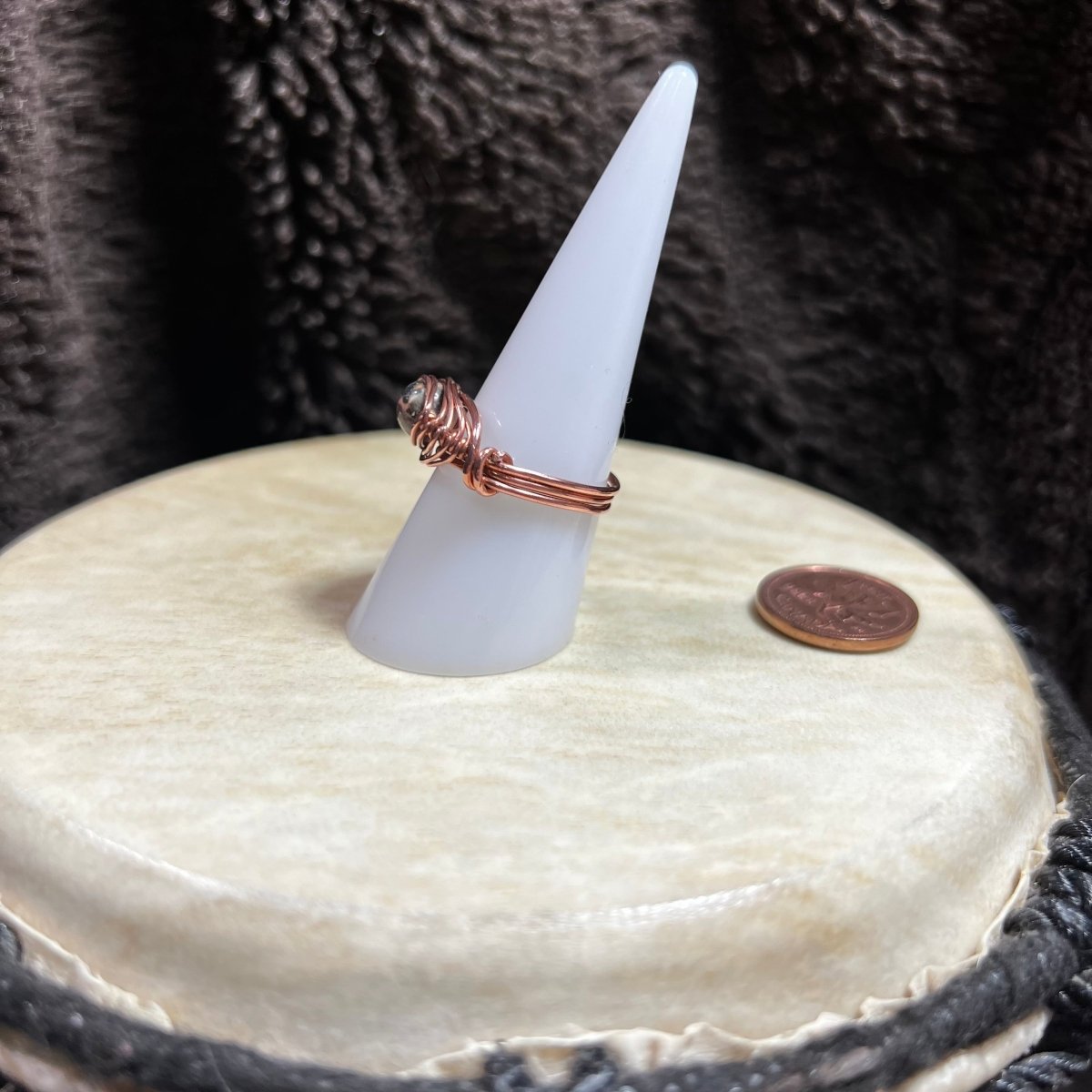 Ring on a cone-shaped stand sitting on a white surface, next to a penny for scale.