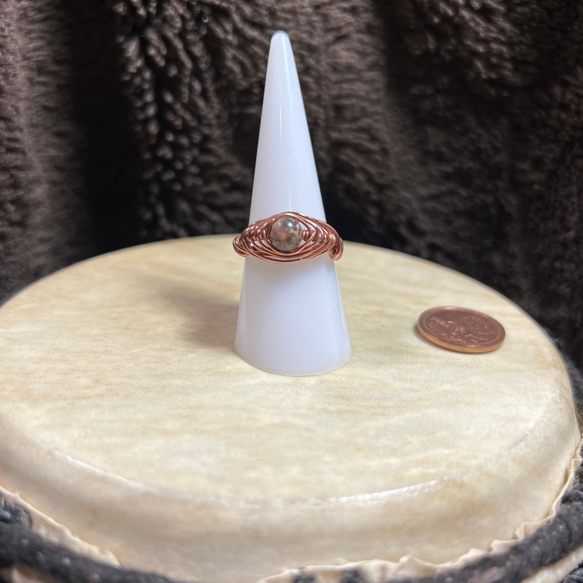 Ring on a cone-shaped stand sitting on a white surface, next to a penny for scale.
