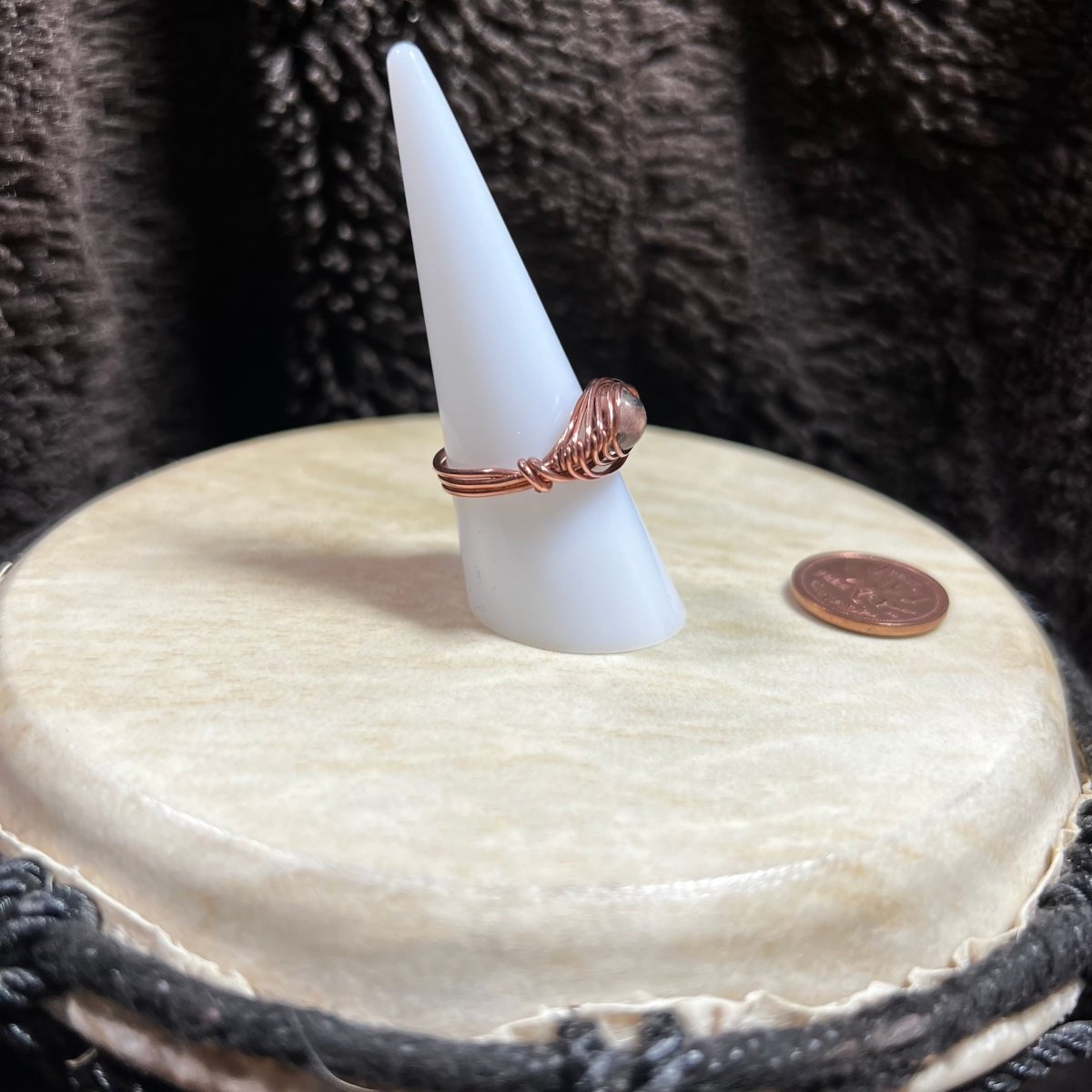 Ring on a cone-shaped stand sitting on a white surface, next to a penny for scale.