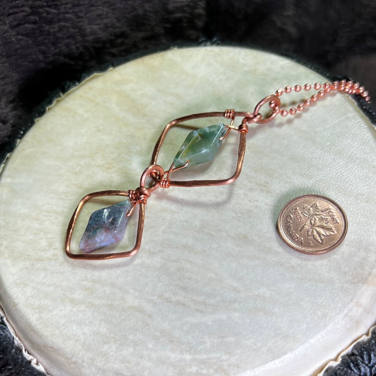 Hand made diamond motif copper necklace with moss agate gemstones on a white surface with a penny for scale.
