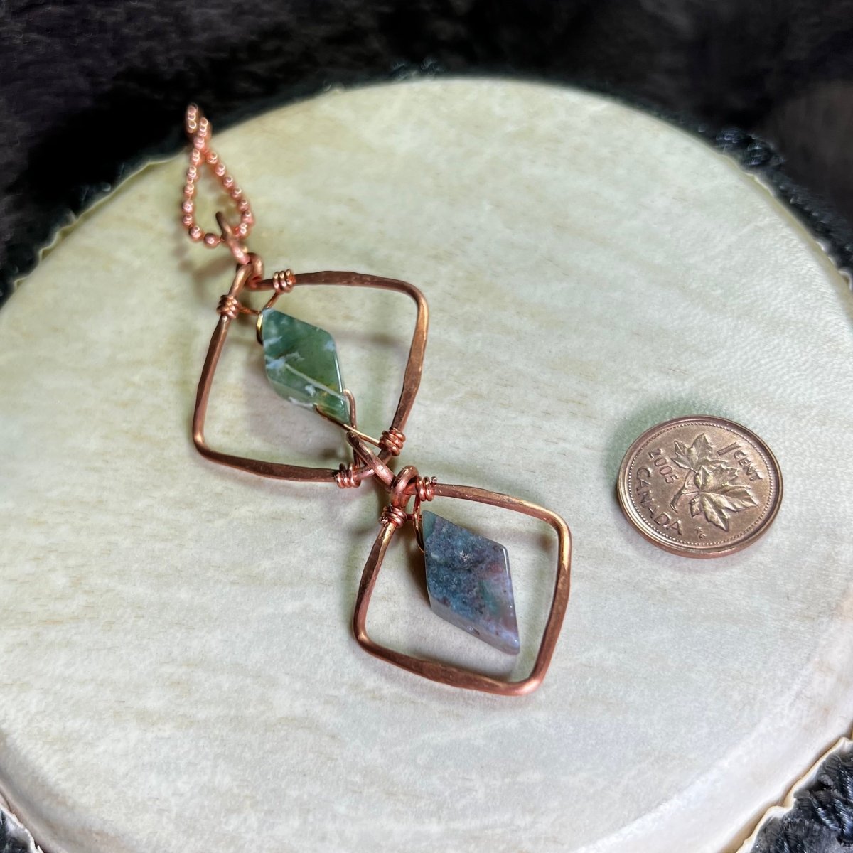 Hand made diamond motif copper necklace with moss agate gemstones on a white surface with a penny for scale.